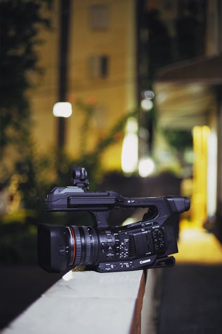 Close-up of a professional video camera on a city balcony at night. Perfect for media and technology themes.